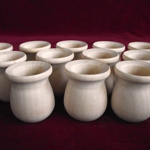 May include: A group of 12 small, wooden cups, all in a light beige color, arranged in a semi-circle on a red surface.