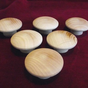 May include: Six wooden knobs in a mushroom shape, with a light brown color and a smooth, slightly textured surface. The knobs are arranged in a semi-circle on a red surface.