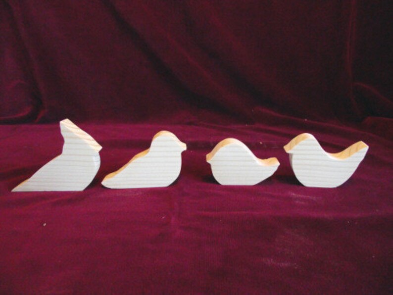 Puede incluir: Cuatro formas de p&aacute;jaros de madera sin terminar, cada una con un dise&ntilde;o diferente. Los p&aacute;jaros est&aacute;n dispuestos en una fila de izquierda a derecha.