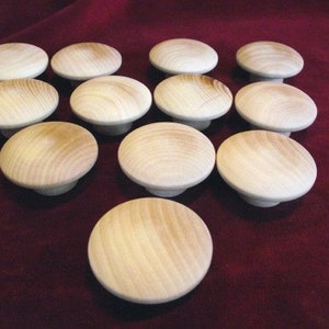 May include: A collection of 12 wooden knobs in a natural finish. The knobs are round and have a smooth surface. They are arranged in a circle on a red surface.