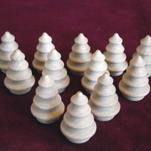 May include: Twelve white wooden Christmas tree ornaments. The ornaments are stacked in a pyramid shape on a red surface.