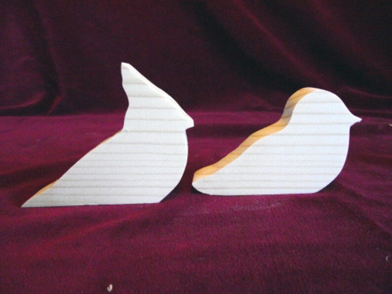 Puede incluir: Dos formas de p&aacute;jaros de madera sin terminar, un cardenal y otro p&aacute;jaro m&aacute;s peque&ntilde;o, sobre un fondo burdeos.