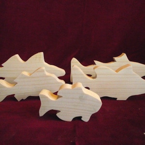 May include: Five unfinished wooden fish shapes of varying sizes. The fish are all made of light-colored wood and have a smooth, sanded finish.