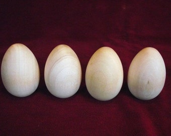 May include: Four wooden eggs, each with a smooth, light brown finish, are arranged in a row on a dark red surface.