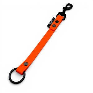 May include: A bright orange strap featuring a black metal swivel snap hook at one end and a black metal O-ring at the other. The strap is secured with two black rivets near the hook and one near the ring. A small black tag reads DINOS.