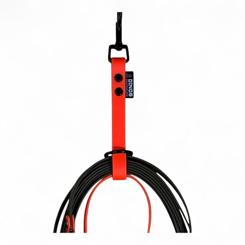 May include: A bright red strap with a black metal hook at the top and a black metal ring at the bottom. The strap features two black rivets and a small black tag with the white text DINOS. A coiled black cord is secured by the red strap.