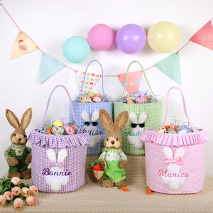 May include: Easter-themed baskets in blue, green, and pink gingham patterns, each with a bunny applique and a name. The baskets are filled with colorful eggs and decorative grass. Plush bunny figures and balloons complete the festive scene.