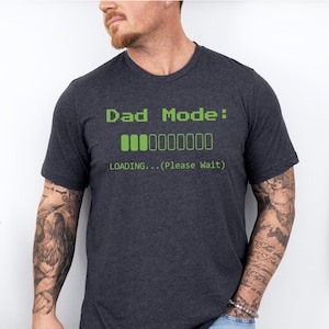 May include: A dark heather grey t-shirt with the text "Dad Mode: LOADING... (Please Wait)" and a green progress bar.