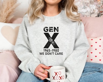 May include: A gray sweatshirt with the text "GEN X 1965-1980 WE DON'T CARE" printed on the front. The person is holding a white mug with the text "XOXO" printed on it.