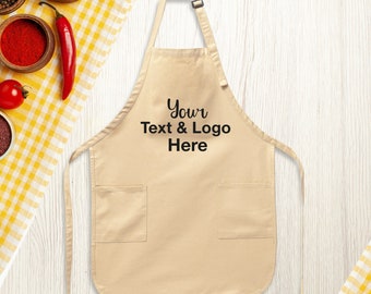May include: A tan apron with two front pockets and adjustable neck strap. The apron has the text "Your Text & Logo Here" printed in black. The apron is displayed on a white wooden surface with a yellow and white checkered cloth.