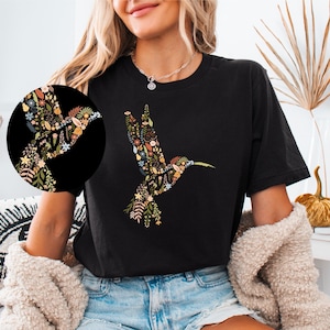 May include: Black t-shirt with a floral hummingbird design. The hummingbird is made up of various flowers and leaves in shades of blue, green, yellow, and orange.