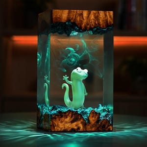 May include: A rectangular resin art piece featuring a light green cartoon lizard inside a clear block. The top and bottom are made of wood with a dark blue-green resin. The lizard is waving, and the piece has a glowing effect.