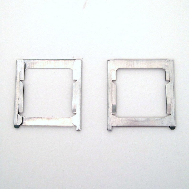 Pu&ograve; includere: Due cornici quadrate in metallo argentato con apertura rettangolare. Ogni cornice ha una serie di piccole linguette e intagli lungo i bordi. Le cornici sono su sfondo bianco.