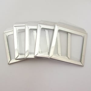 May include: A set of five rectangular silver-toned metal slide mounts with open centers. Each mount features a smooth, reflective finish and a beveled frame design, arranged in a slightly overlapping fan pattern against a plain background.