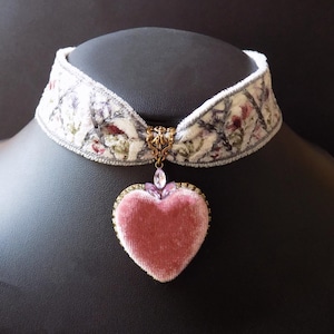 Soft pink velvet heart choker necklace on winter white embroidered velvet ribbon with floral detailing and lilac crystal accents, displayed on a black mannequin bust.