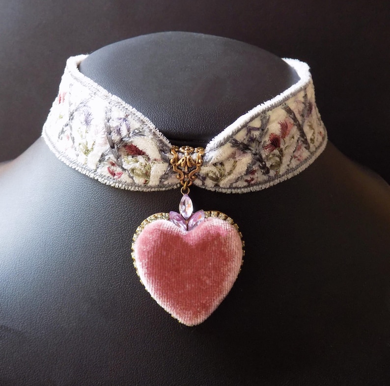 Soft pink velvet heart choker necklace on winter white embroidered velvet ribbon with floral detailing and lilac crystal accents, displayed on a black mannequin bust.