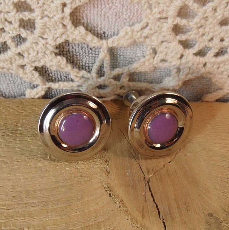 Peut inclure: Une paire de boutons de manchette vintage argent&eacute;s de forme circulaire. Chaque bouton de manchette pr&eacute;sente un centre lavande, un anneau cuivr&eacute; et un bord ext&eacute;rieur argent&eacute;. Les boutons de manchette sont pr&eacute;sent&eacute;s sur une surface en bois.