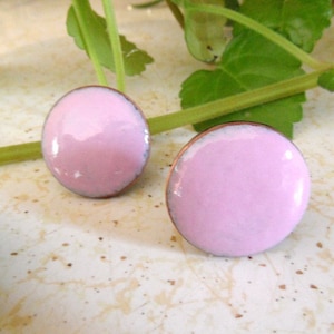 May include: A pair of pink enamel earrings with a copper backing. The earrings are round and have a glossy finish.