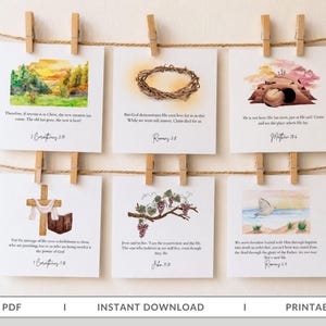 May include: Six square white cards with watercolor illustrations and Bible verses, suspended by wooden clothespins on two horizontal twine strings. The designs feature a landscape, a crown of thorns, an empty tomb, a cross, grapes, and a dove.