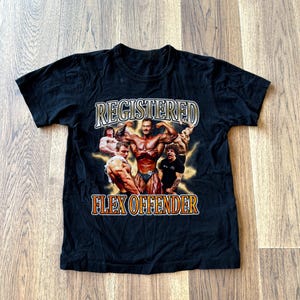May include: Black t-shirt with a graphic print of bodybuilders and the text "Registered Flex Offender".