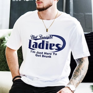 Puede incluir: Camiseta blanca con un gráfico azul que dice "Not Tonight Ladies I'm Just Here To Get Drunk".