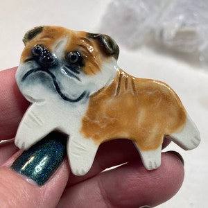 May include: A ceramic bulldog figurine with brown and white fur. The figurine is hand-painted with details on the face and body.