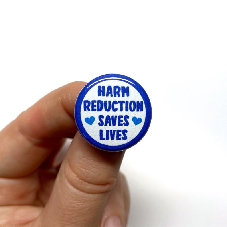 Puede incluir: Un bot&oacute;n azul y blanco con el texto "Harm Reduction Saves Lives" y dos corazones azules.