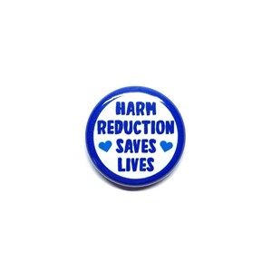 Puede incluir: Un bot&oacute;n azul y blanco con el texto "Harm Reduction Saves Lives" y dos corazones azules.