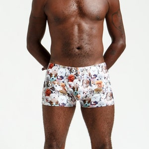 May include: A man wearing white boxer shorts with a colorful print of dogs. He is wearing black boots and has a necklace around his neck.