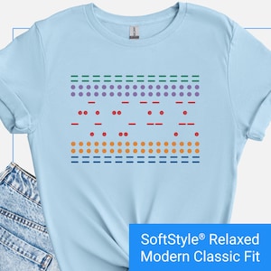 May include: Light blue t-shirt with a graphic design of a code in braille. The code is in different colors, including green, purple, red, orange, and blue. The text "SoftStyle Relaxed Modern Classic Fit" is at the bottom of the image.