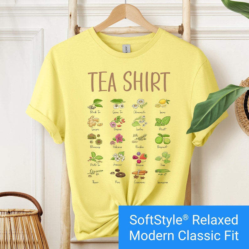 Bright yellow t-shirt featuring a colorful illustrated grid of tea ingredients like mint, ginger, chamomile, and berries with large text that reads “Tea Shirt” at the top in brown lettering.