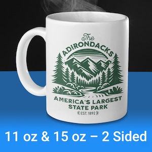 May include: White ceramic mug with a green graphic design of mountains, trees, and a river. The text "The Adirondacks America's Largest State Park Est. 1892" is printed on the mug. The mug is available in 11 oz and 15 oz sizes and is two-sided.