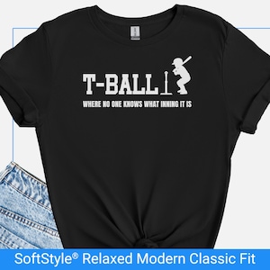 Op de afbeelding: Zwart T-shirt met de witte woorden "T-BALL" en de zin "WHERE NO ONE KNOWS WHAT INNING IT IS". Een wit silhouet van een slagman staat rechts. Het shirt is een SoftStyle Relaxed Modern Classic Fit.