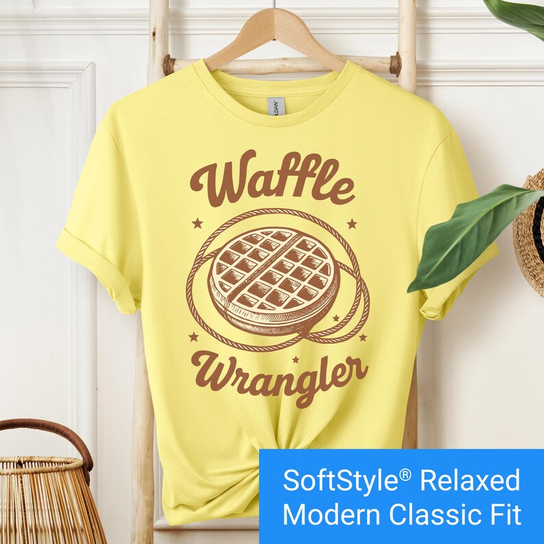 Bright yellow t-shirt with a brown vintage-style graphic of a waffle encircled by a rope lasso, with the words "Waffle Wrangler" above and below the design.