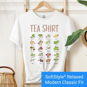 White t-shirt featuring a colorful illustrated grid of tea ingredients like mint, ginger, chamomile, and berries with large text that reads “Tea Shirt” at the top in brown lettering.