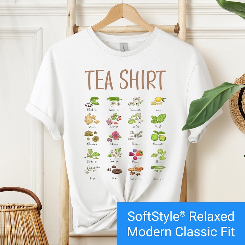 White t-shirt featuring a colorful illustrated grid of tea ingredients like mint, ginger, chamomile, and berries with large text that reads “Tea Shirt” at the top in brown lettering.