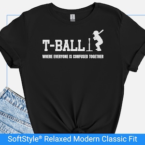 Op de afbeelding: Zwart t-shirt met witte tekst en afbeelding. De tekst luidt "T-BALL" boven "WHERE EVERYONE IS CONFUSED TOGETHER". Een silhouet van een slagman is afgebeeld. Het shirt is een SoftStyle Relaxed Modern Classic Fit.