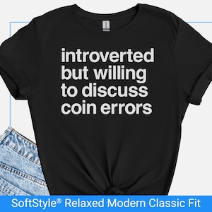 May include: Black t-shirt with white text: "introverted but willing to discuss coin errors." The shirt has a relaxed, modern classic fit. The bottom of the shirt is knotted. Denim jeans are visible in the lower left corner.