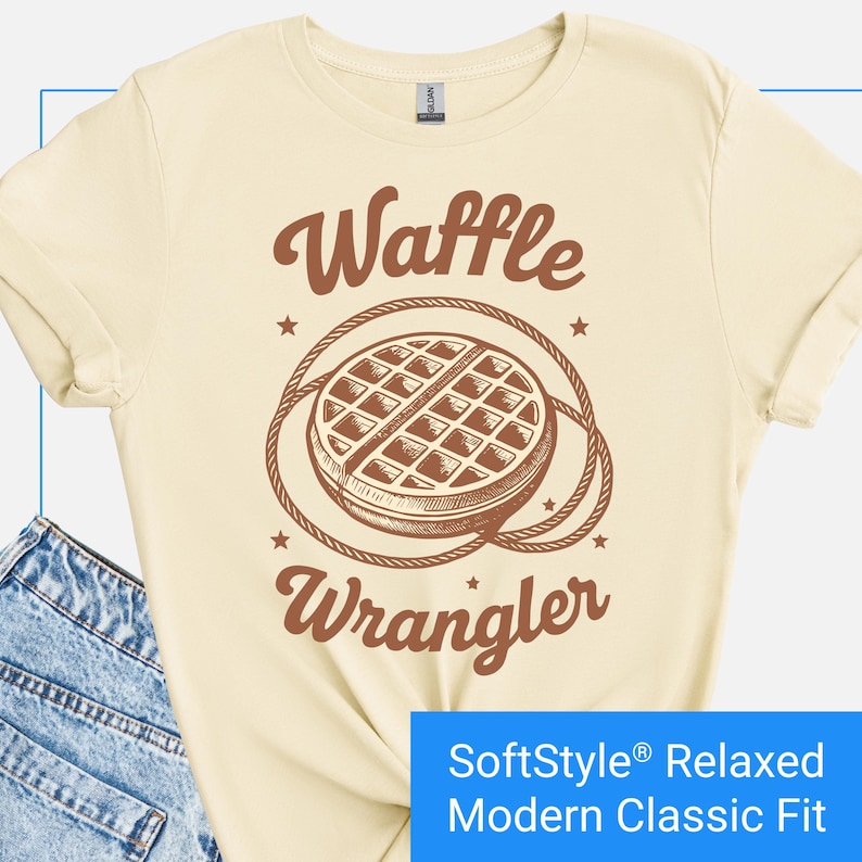 Cream color t-shirt with a brown vintage-style graphic of a waffle encircled by a rope lasso, with the words "Waffle Wrangler" above and below the design.