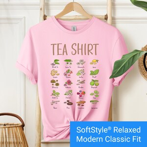 Light pink t-shirt featuring a colorful illustrated grid of tea ingredients like mint, ginger, chamomile, and berries with large text that reads “Tea Shirt” at the top in brown lettering.
