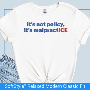 Puede incluir: Camiseta blanca con el texto "it's not policy, it's malpractice" en azul y rojo. La camiseta tiene un corte relajado y está hecha de un material suave. La camiseta es un clásico moderno.