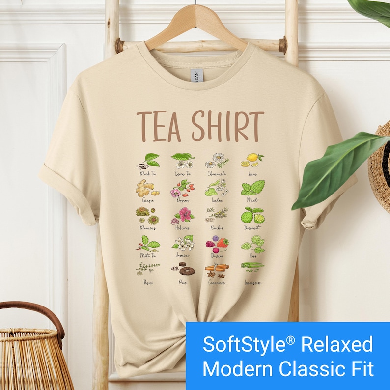 Sand color t-shirt featuring a colorful illustrated grid of tea ingredients like mint, ginger, chamomile, and berries with large text that reads “Tea Shirt” at the top in brown lettering.