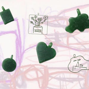 Peut inclure: Plusieurs pendentifs vert foncé de formes variées : un rectangle, un cœur, un cercle et une forme abstraite. L'image comprend également un dessin au trait d'une plante en pot avec l'étiquette "mustard" et une illustration sur le thème du vin avec les mots "wine night".