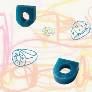 Peut inclure: Modèles de cire de bagues bleu sarcelle et dessins au trait bleus de bagues sur un fond coloré. Les modèles de cire sont solides et géométriques, tandis que les dessins présentent divers motifs, dont un cœur et un soleil.