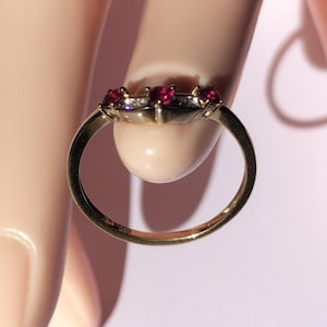 May include: A gold ring with three red gemstones and small white gemstones. The ring has a polished gold band. The gemstones are set in a decorative setting, possibly vintage.