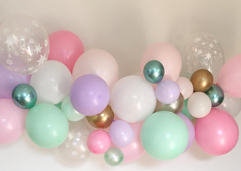 May include: A collection of pastel-colored balloons in pink, white, mint green, and lavender. Some balloons are clear with snowflake patterns. Metallic gold and teal balloons add accents. Perfect for a party or celebration.