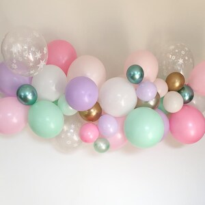May include: A collection of colorful balloons in various sizes and shades, including pink, purple, green, and white. Some balloons are clear with snowflake patterns, creating a festive and celebratory atmosphere.