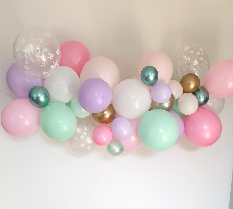May include: A collection of colorful balloons in various sizes and shades, including pink, purple, green, and white. Some balloons are clear with snowflake patterns, creating a festive and celebratory atmosphere.