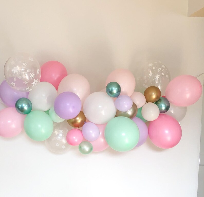 May include: A collection of pastel-colored balloons in pink, white, green, and purple, with some featuring star patterns. Metallic gold and teal balloons add accents. The balloons are arranged in a decorative cluster.