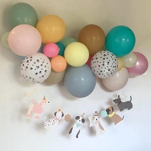 May include: A vibrant balloon display in pastel shades of pink, yellow, and blue. The arrangement includes paw print balloons and a dog-themed banner with party hats. Ideal for a dog-themed birthday celebration.
